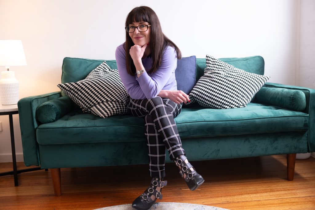 sexologist lauren muratore sitting on green couch with legs crossed and black leather buckle boots
