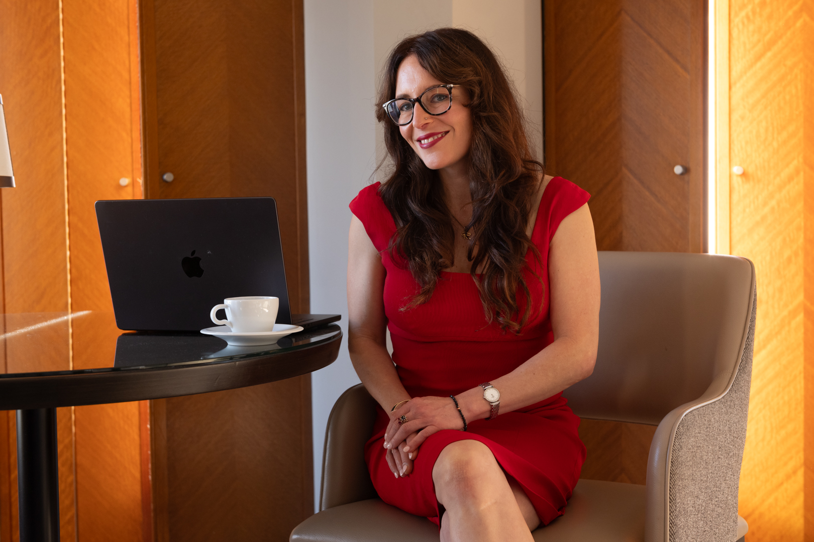 Sexologist Lauren Muratore wearing a red dress sitting at a desk with laptop and cup of tea